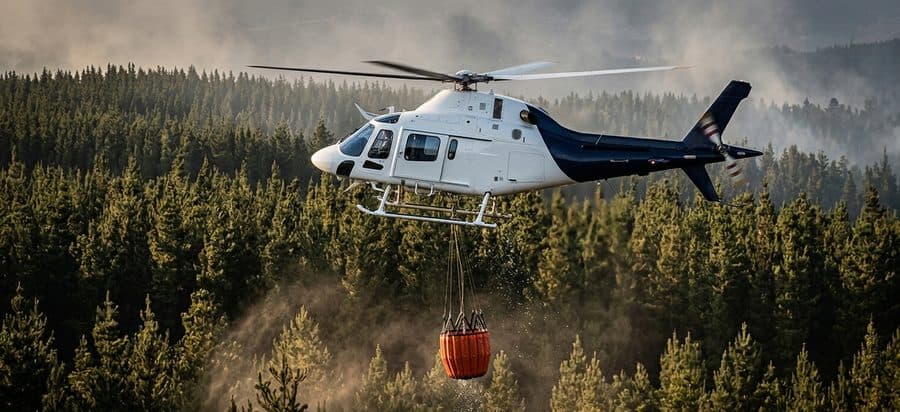Helicopter with a water bucket over a smoky forest